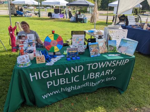 table with a selection of materials at a farmer's market with a smiling librarian