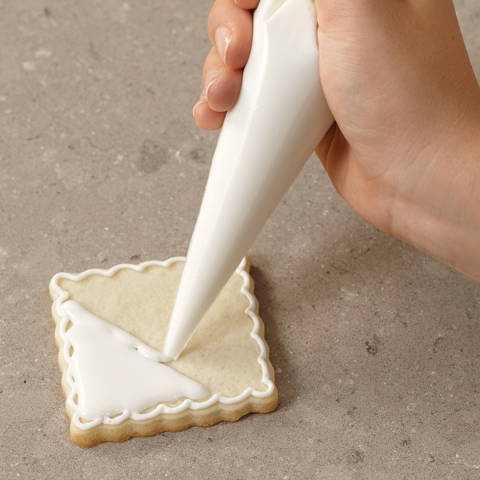 a hand piping royal frosting onto a square cookie