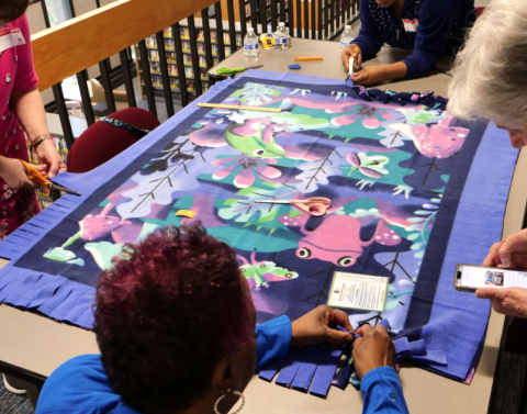 group of four cutting and tying a fleece comfort blanket